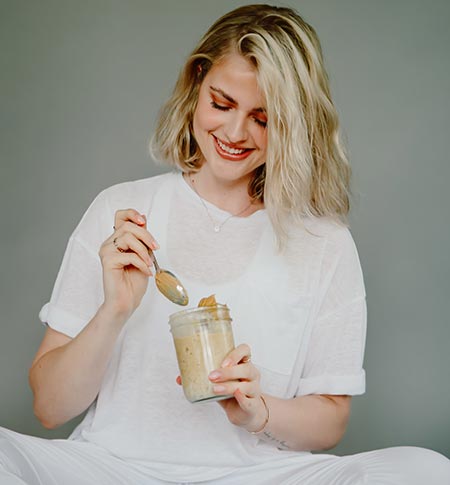 young sitting lady dipping spoon into peanut butter jar depicting free consultation for nutrition coach